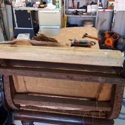 Restoration in progress on a vintage armchair, showing the stripped timber frame, hessian webbing, and tools laid out during reupholstery in a Bexley workshop