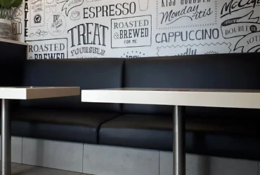 Freshly reupholstered black booth seating at McDonald’s, blending seamlessly with the graphic café-style wall and bright tiled floor.