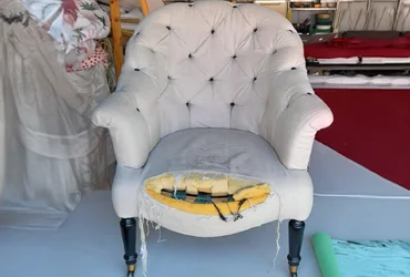 Traditional tub chair with tufted button back and rolled arms, showing worn upholstery and exposed seat padding in a Bexley workshop before restoration.