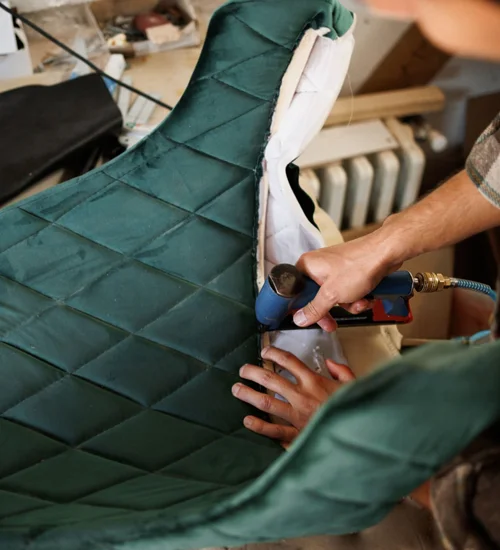 Qualified upholstery professional using a staple gun to reupholster a green diamond stitched lounge chair